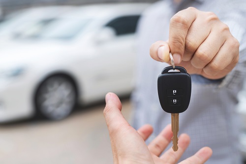 Individual at car dealership handing over car keys to their new owner