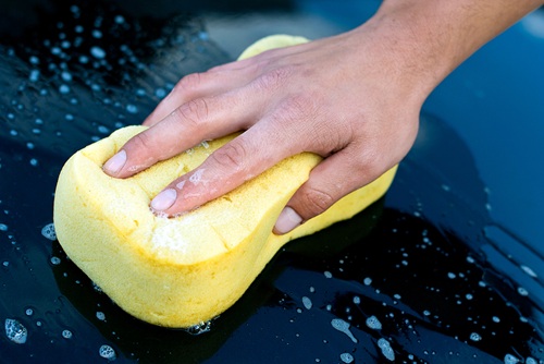 Hand washing a car with yellow sponge