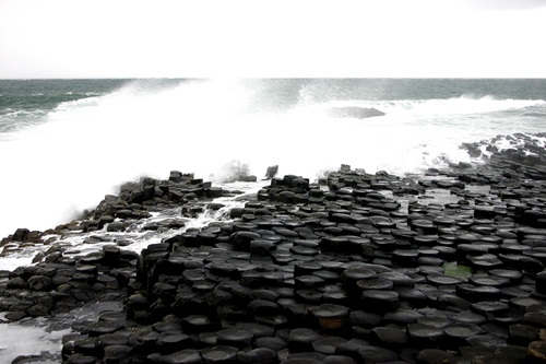Waves crashing against dark hexagonal basalt columns on a rocky shore.
