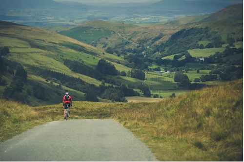 Cyclist on a rural road riding through green rolling hills and valleys.