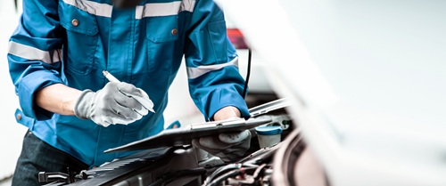 person standing in front of an open car bonnet with a pen and clipboard during an MOT inspection