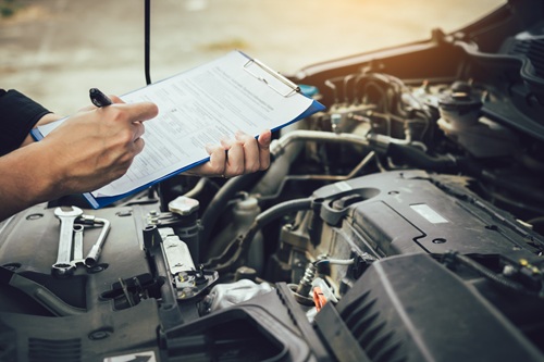 Person with a clipboard and checklist at the open bonnet of a car